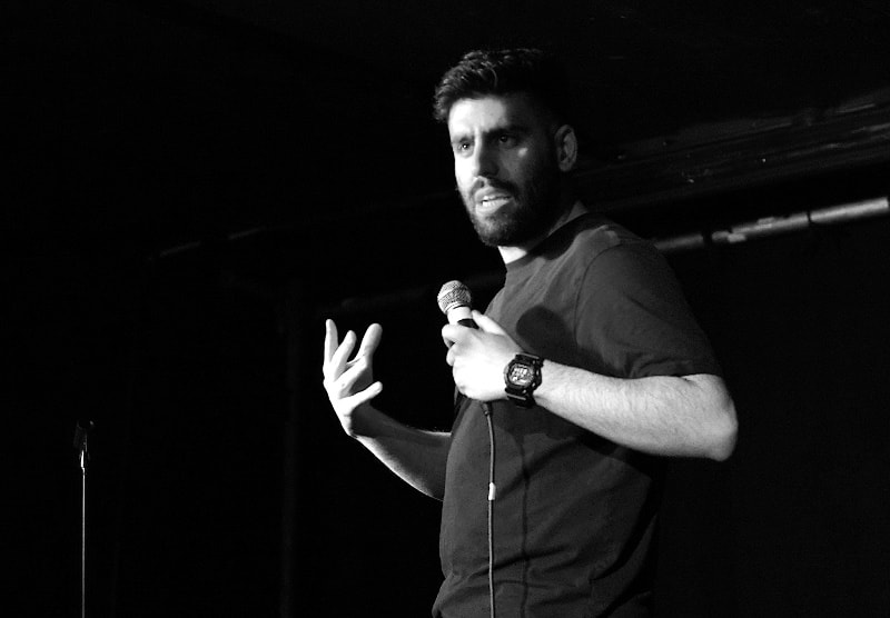 Adam Coumas Comedian holding a Mic